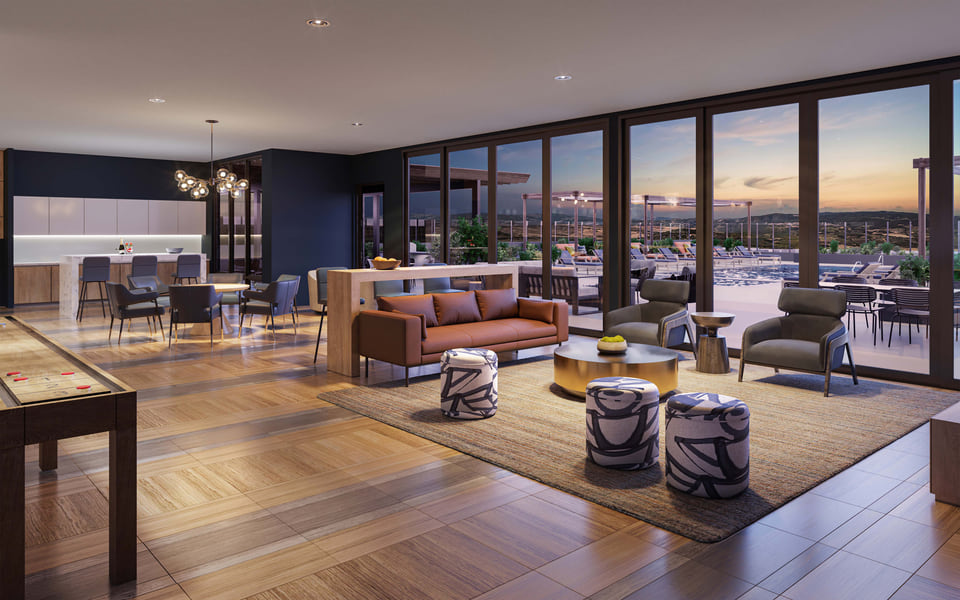 Interior rendering of a residential club room at dusk with a shuffleboard table, kitchen island bar seating, and floor-to-ceiling windows opening onto a rooftop pool deck