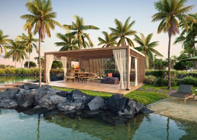 A charming Hawaiian cabana with bamboo walls and a thatched roof, set on a sandy beach. Surrounded by vibrant tropical flowers and palm trees, it overlooks the clear turquoise ocean. The sky above is a bright, cloudless blue.